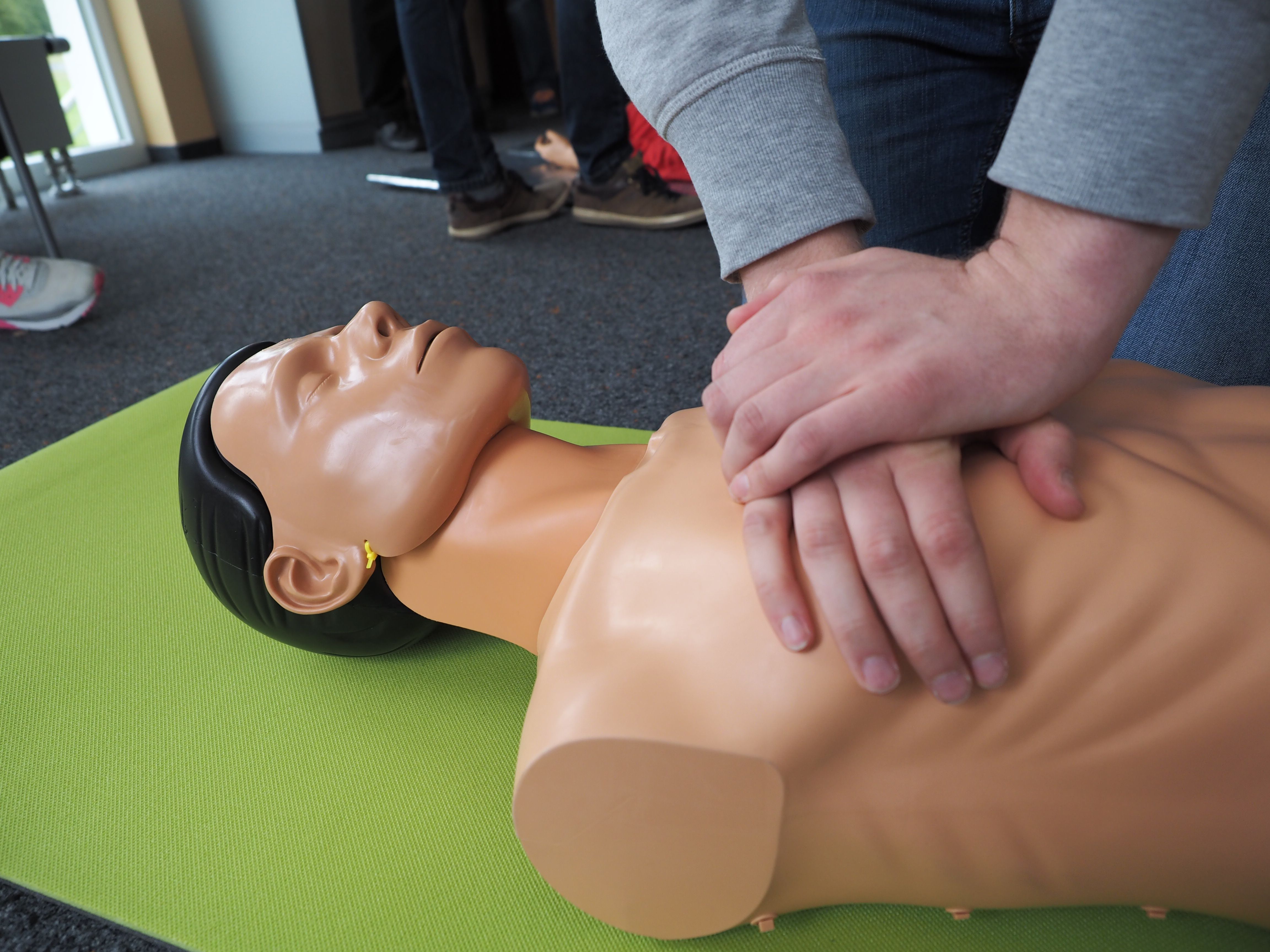 Foto: Eine DRK-Ausbilderin führt den Teilnehmern die Herzdruckmassage an einem Dummy vor.